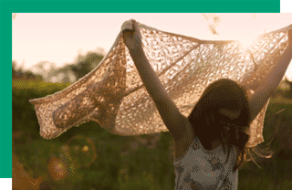 Person holding sweater with arms held high and sunlight shining in the background