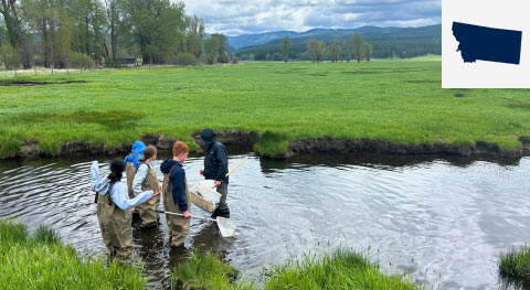 Students wearing waders and surveying creek with small map of Montana in top right corner