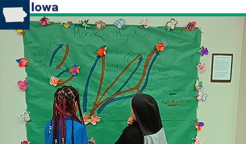 Students studying monarch migration poster; small map of Iowa