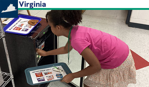 Student holding tray and reaching into small refrigerator; small map of Virginia
