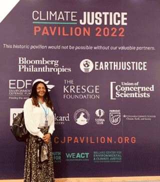 Person standing in front of Climate Justice Pavilion 2022 banner