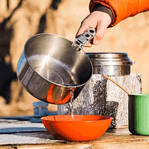 Close up of water being poured from pot into bowl at campsite