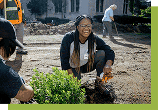 Person smiling and crouched down next to small plant being planted